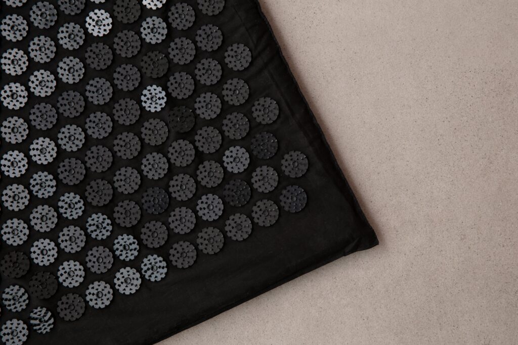 Detailed view of a black acupuncture mat on a neutral background, promoting relaxation and wellness.